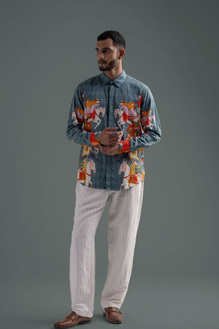 Man wearing the blue Kirtharjuna shirt with white trousers, full length front view, hands clasped