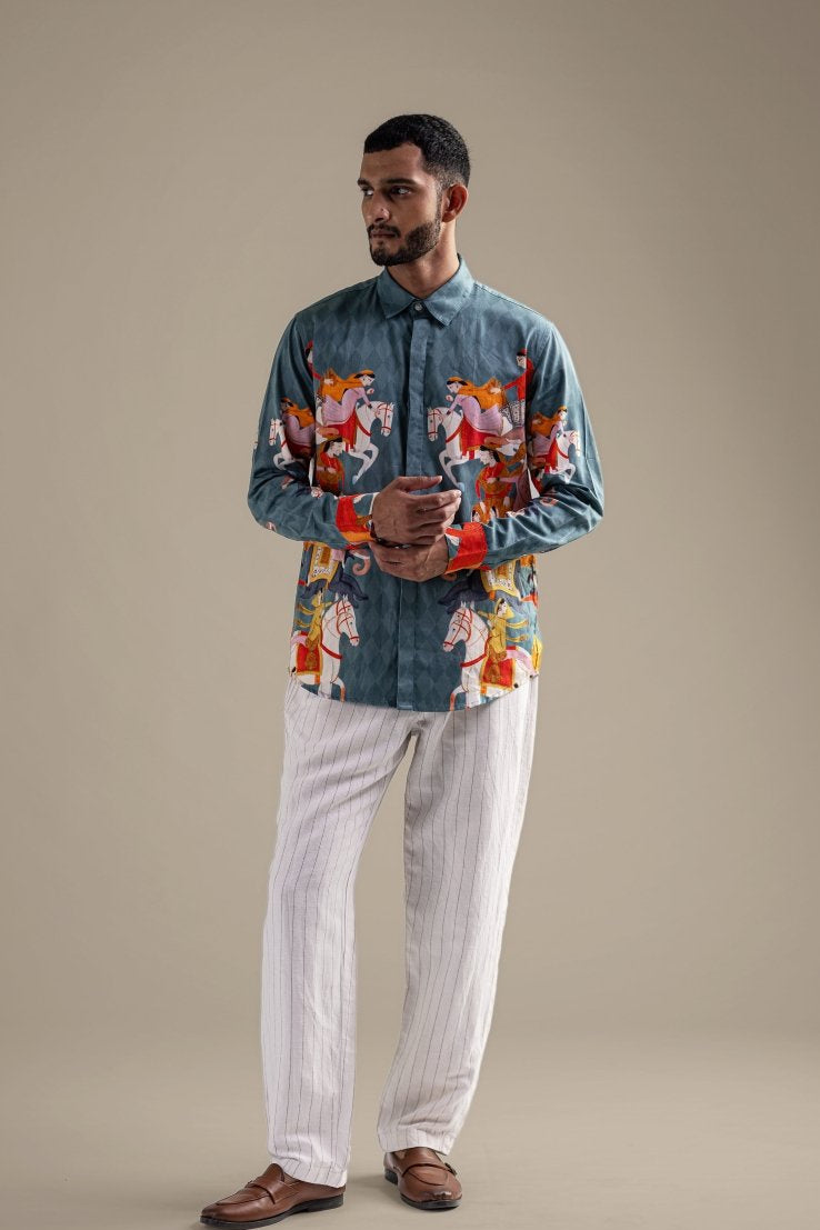 Man wearing the Kirtharjuna shirt with white trousers, full length front view, hands clasped