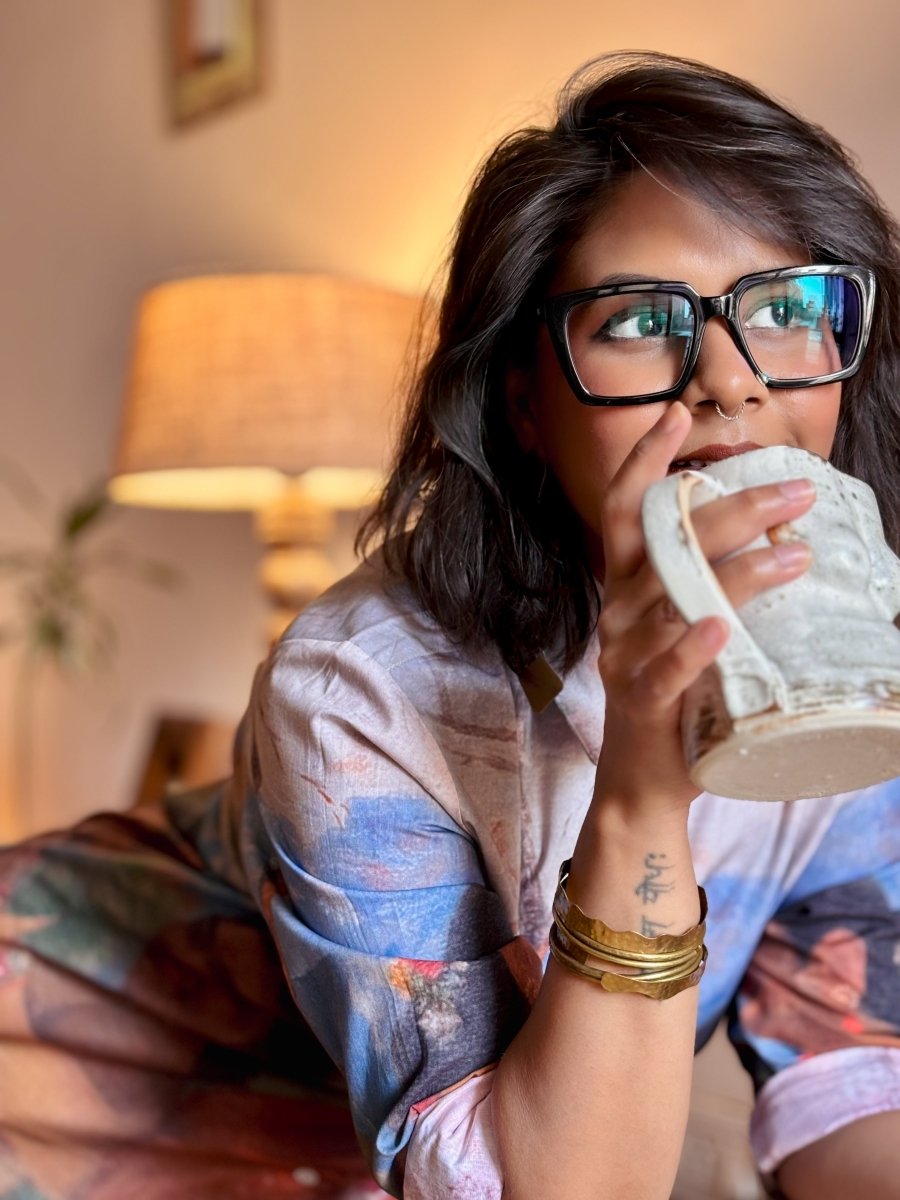 Woman wearing the Shakuntala shirt, resting on a sofa and drinking from a mug, close view