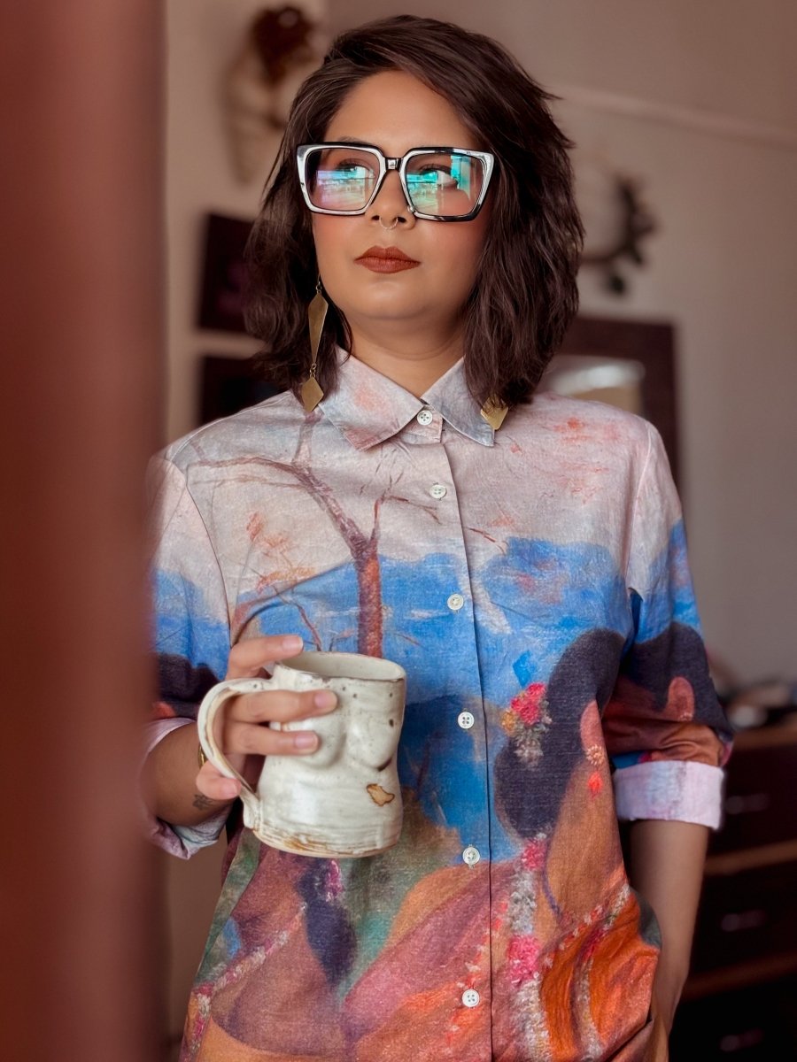 Woman wearing the Shakuntala shirt, holding a mug, standing by a doorway, front view