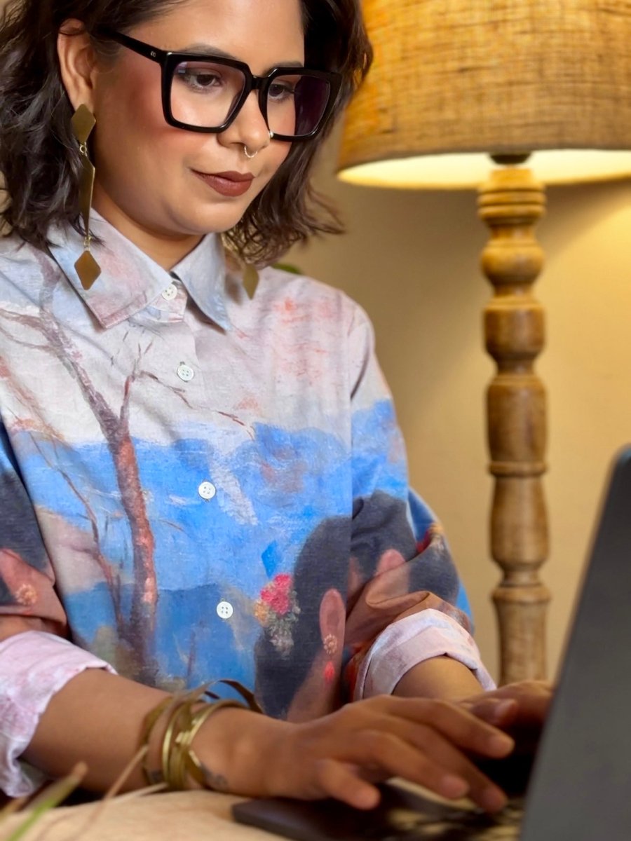 Woman wearing the Shakuntala shirt, working at a laptop, seen from the front with sleeves rolled up
