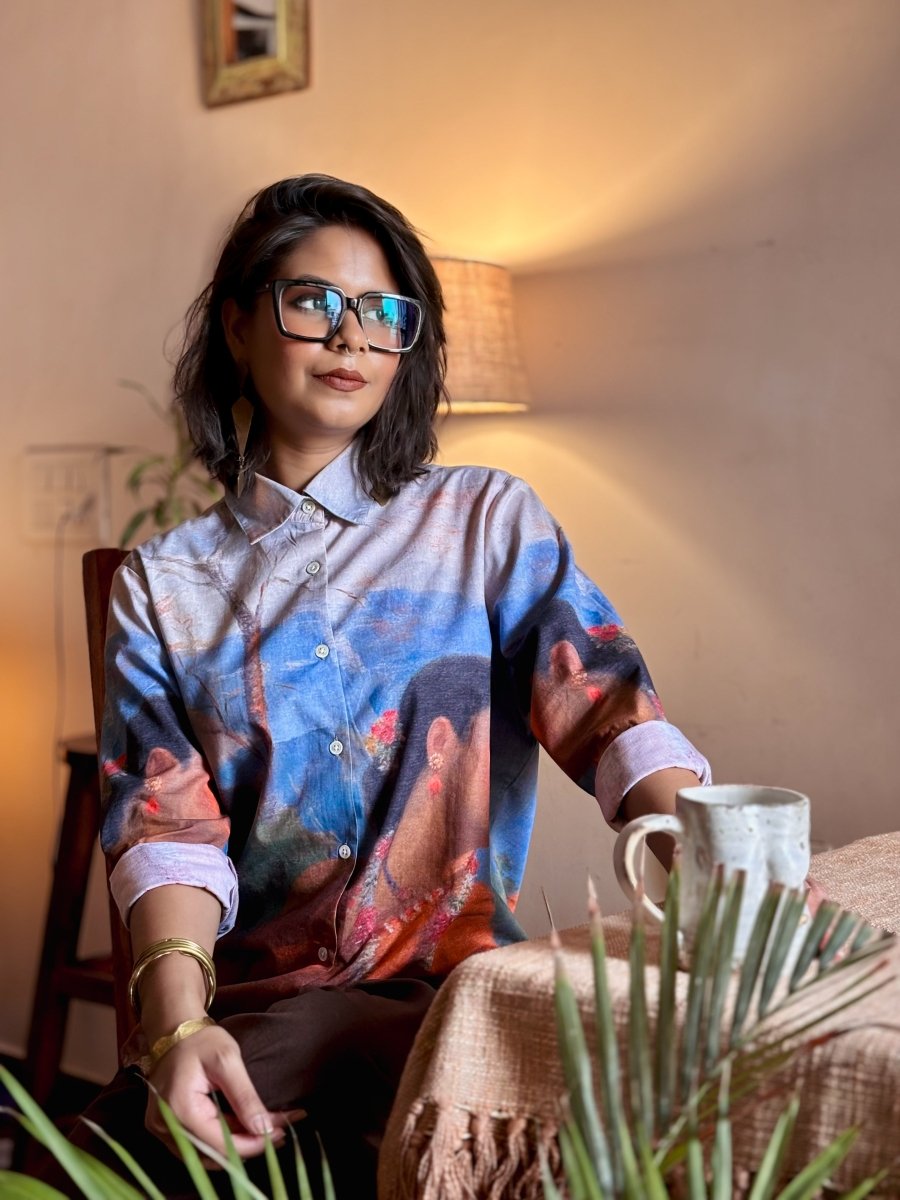 Woman wearing the Shakuntala shirt, seated on a chair with a mug, front view